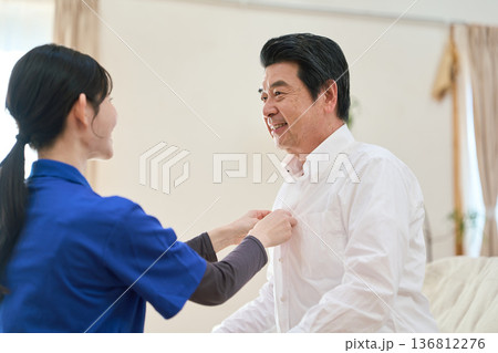訪問介護でシャツのボタンを留めるアジア人介護士 136812276