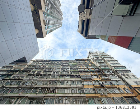 Looking up at contrasting modern and old apartment buildings against a cloudy sky 136812393