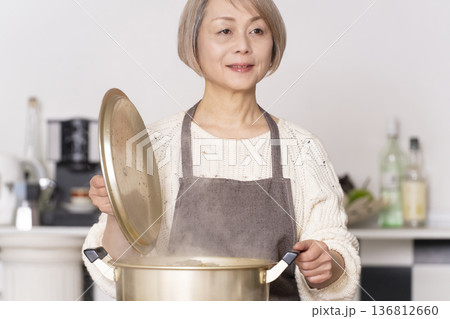 キッチンで豚汁を作りお椀に盛り付けるシニア女性 136812660