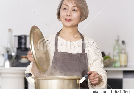 キッチンで豚汁を作りお椀に盛り付けるシニア女性 136812661