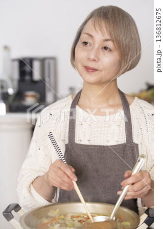 キッチンで豚汁を作りお椀に盛り付けるシニア女性 136812675