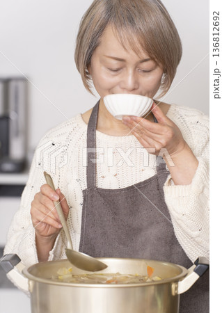 キッチンで豚汁を作りお椀に盛り付けるシニア女性 136812692