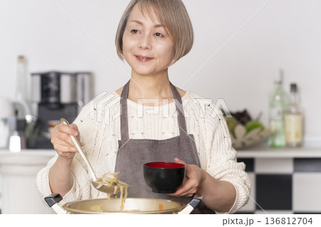 キッチンで豚汁を作りお椀に盛り付けるシニア女性 136812704