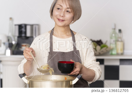 キッチンで豚汁を作りお椀に盛り付けるシニア女性 136812705