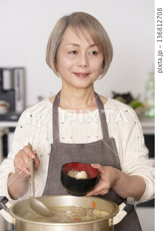 キッチンで豚汁を作りお椀に盛り付けるシニア女性 136812708
