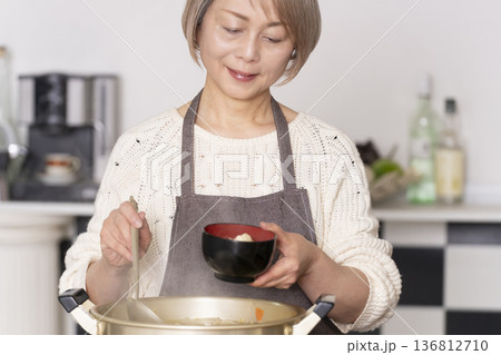 キッチンで豚汁を作りお椀に盛り付けるシニア女性 136812710