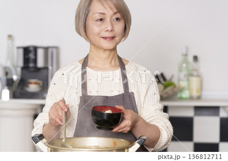 キッチンで豚汁を作りお椀に盛り付けるシニア女性 キッチンで豚汁を作りお椀に盛り付けるシニア女性 136812711