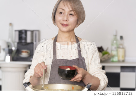 キッチンで豚汁を作りお椀に盛り付けるシニア女性 136812712