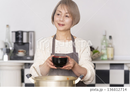 キッチンで豚汁を作りお椀に盛り付けるシニア女性 136812714