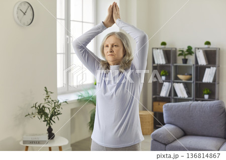Healthy home yoga workout, meditation of senior woman, standing with hands up in namaste gesture Healthy home yoga workout, meditation of senior woman, standing with hands up in namaste gesture 136814867