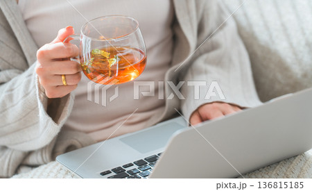 ソファーに座り紅茶を飲みながらパソコンを見る女性 136815185