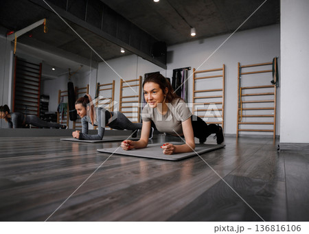 Fitness training session with young women doing planks in a gym studio with modern equipment Fitness training session with young women doing planks in a gym studio with modern equipment 136816106