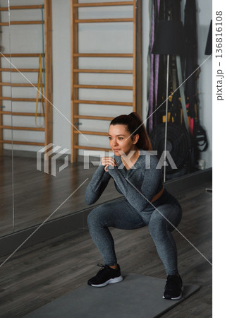 Woman exercises in gym while doing squats during morning workout session 136816108