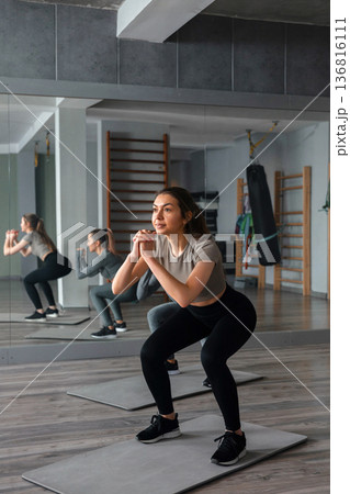 Woman practicing squats in gym during workout session with focus on fitness routine and group training Woman practicing squats in gym during workout session with focus on fitness routine and group training 136816111
