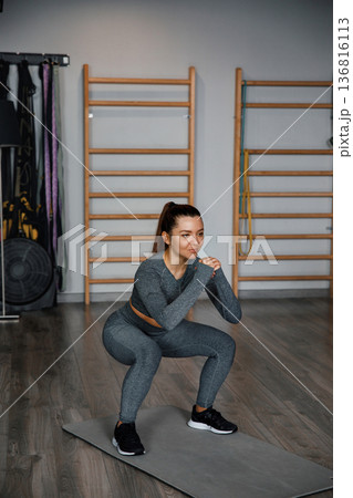 Woman performs squats in gym during training session at indoor fitness center 136816113