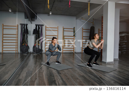 Women workout in gym doing squats on mats during morning training session for fitness 136816114