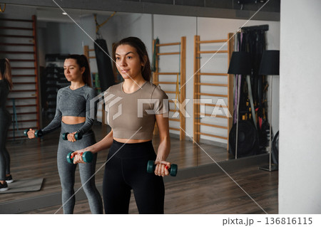 Fitness training session with young women lifting weights in gym environment Fitness training session with young women lifting weights in gym environment 136816115