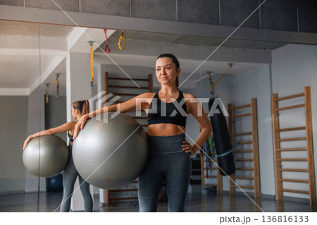 Woman in gym holding a fitness ball and preparing for her workout routine with focus on health and fitness Woman in gym holding a fitness ball and preparing for her workout routine with focus on health and fitness 136816133