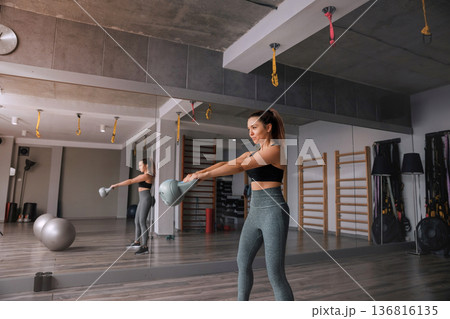 Woman training with kettlebell in modern gym space during afternoon Woman training with kettlebell in modern gym space during afternoon 136816135