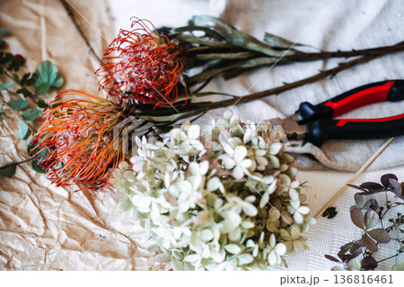 Flowers and florist tools rest on wrinkled paper and light fabric. hybrid floral design, mixed textures, dried and fresh flowers, botanical contrast, modern floristry, floral preservation Flowers and florist tools rest on wrinkled paper and light fabric. hybrid floral design, mixed textures, dried and fresh flowers, botanical contrast, modern floristry, floral preservation 136816461