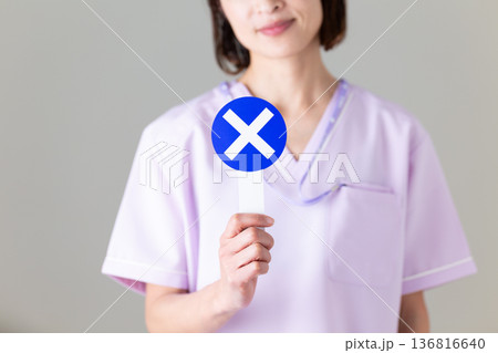 バツのプレートを持つ医療用スクラブ姿のミドル女性看護師 バツのプレートを持つ医療用スクラブ姿のミドル女性看護師 136816640