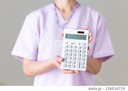 電卓を持つ医療用スクラブ姿のミドル女性看護師 136816719