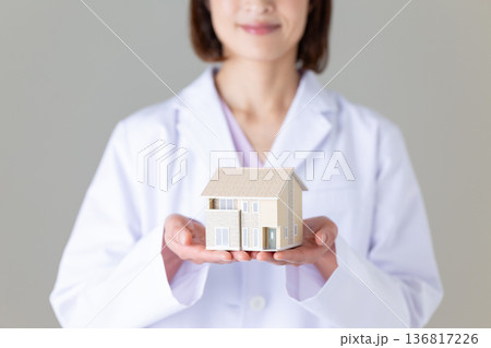 住宅模型を持つ白衣姿のミドル女性医師 136817226