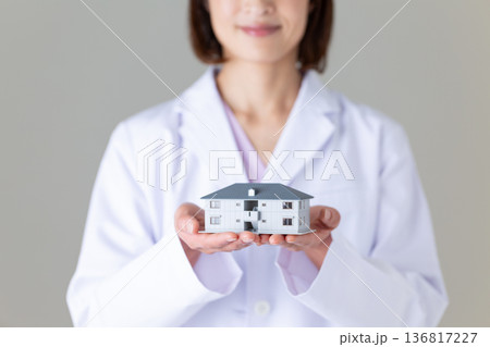 住宅模型を持つ白衣姿のミドル女性医師 136817227