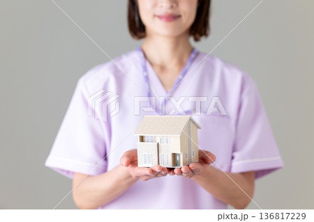 住宅模型を持つ医療用スクラブ姿のミドル女性看護師 136817229