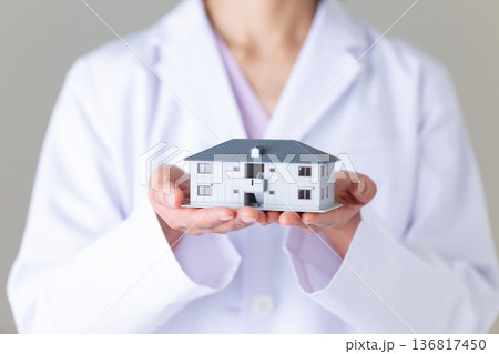 住宅模型を持つ白衣姿のミドル女性医師 136817450