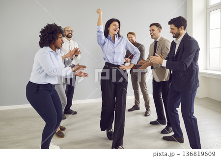 Company employees celebrating success congratulating female colleague indoors. 136819609