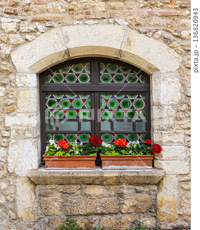Stone wall featuring arched medieval window with geraniums 136820943
