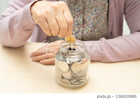 Retired elderly woman putting coins money in piggy bank and worry about monthly expenses and treatment fee payment. 136820980