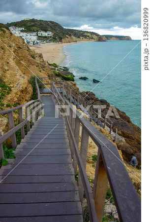 Wooden steps down rocky cliffs to ocean Salema Beach Portugal 136820999