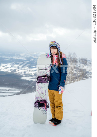 ゲレンデの頂上でスノーボードをする若い女性 136821904
