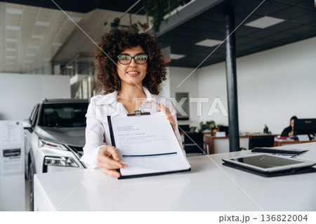 Fulfill the document of buying. Female employee is in the car retail shop 136822004