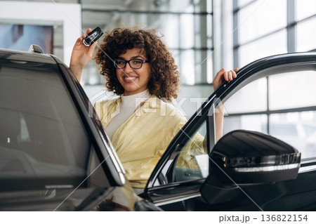 In the retail shop, near car and with keys. Pretty woman is smiling In the retail shop, near car and with keys. Pretty woman is smiling 136822154