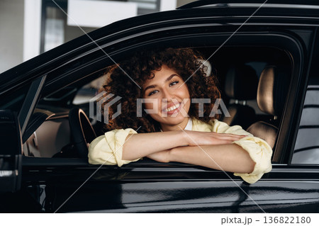 Looking through the opened window and smiling. Happy woman is sitting in the car Looking through the opened window and smiling. Happy woman is sitting in the car 136822180