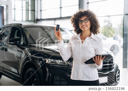 Curly hair, holding keys. Female employee is in the car retail shop 136822196