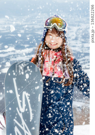 ゲレンデの頂上でスノーボードを楽しむ若い女性 136822266