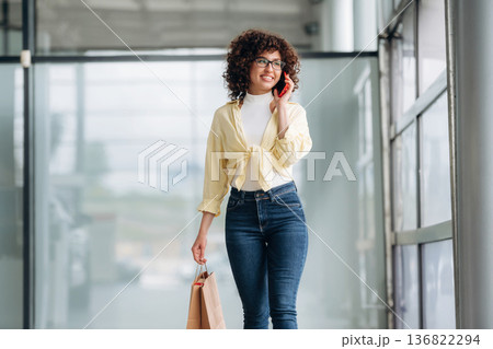 Conversation by using phone. Beautiful woman is standing indoors against blurred wall Conversation by using phone. Beautiful woman is standing indoors against blurred wall 136822294