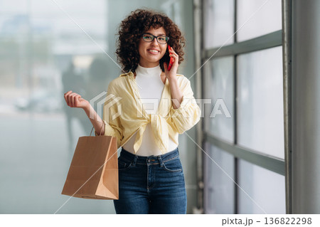 Conversation by using phone. Beautiful woman is standing indoors against blurred wall Conversation by using phone. Beautiful woman is standing indoors against blurred wall 136822298