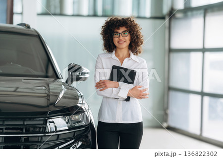 By the black vehicle. Female employee is in the car retail shop By the black vehicle. Female employee is in the car retail shop 136822302