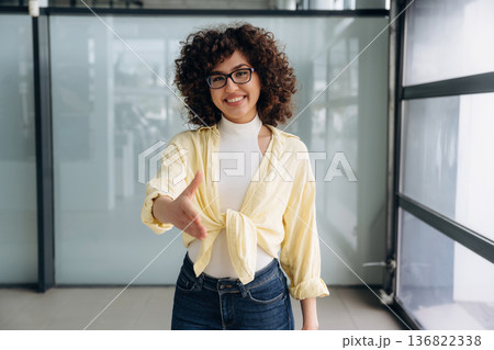 Giving hand to shake. Beautiful woman is standing indoors against blurred wall 136822338