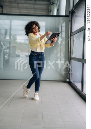 Writing the information while talking by the phone. Beautiful woman is standing indoors against blurred wall 136822344