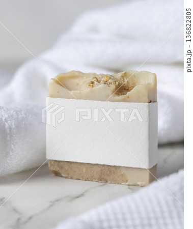 Mockup of beige solid soap bar with blank paper label near white bath towel, personal care packaging 136822805