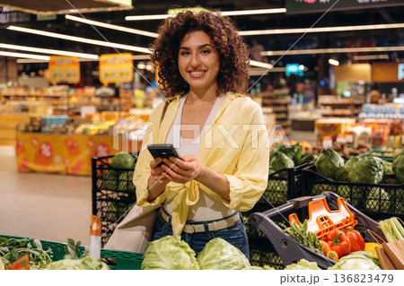 Modern smartphone, holding it. Gorgeous woman is in the grocery store Modern smartphone, holding it. Gorgeous woman is in the grocery store 136823479