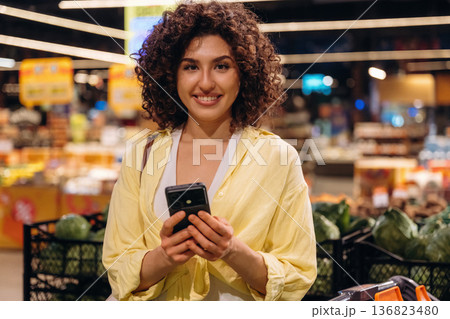 Modern smartphone, holding it. Gorgeous woman is in the grocery store Modern smartphone, holding it. Gorgeous woman is in the grocery store 136823480
