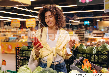 Red smartphone is in hand. Gorgeous woman is in the grocery store 136823496