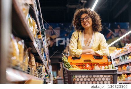 By the shelves with products. Gorgeous woman is in the grocery store By the shelves with products. Gorgeous woman is in the grocery store 136823505